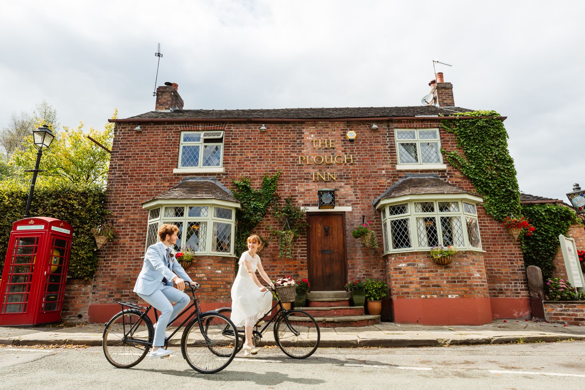 A bride and groom cycling past the front of The Plough Inn